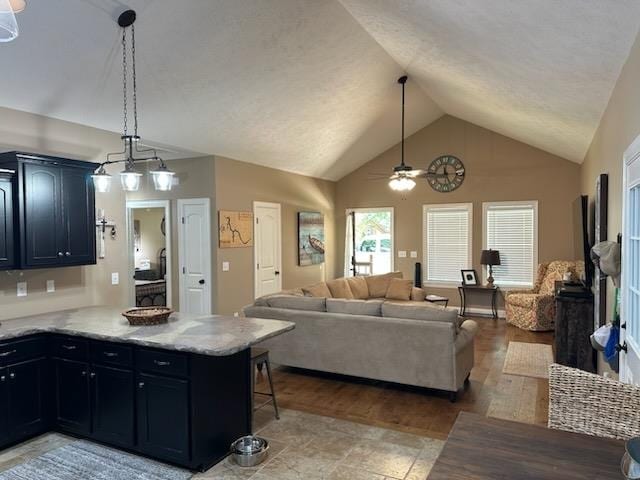 kitchen with ceiling fan with notable chandelier, a kitchen breakfast bar, light stone countertops, lofted ceiling, and light hardwood / wood-style floors