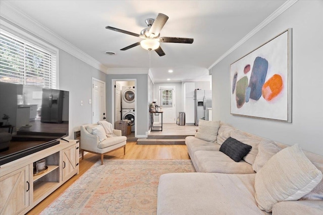 living room with light hardwood / wood-style floors, ceiling fan, crown molding, and stacked washer / dryer