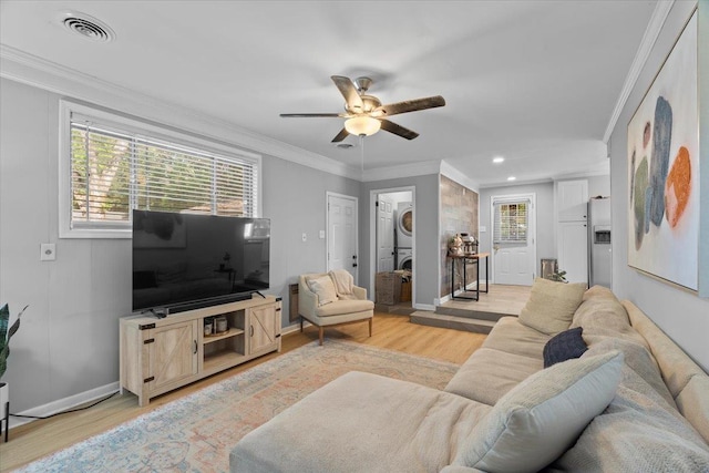 living room featuring light wood-type flooring, stacked washer / drying machine, visible vents, and ornamental molding