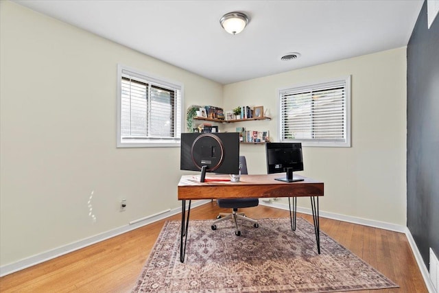 home office with wood finished floors, a healthy amount of sunlight, visible vents, and baseboards