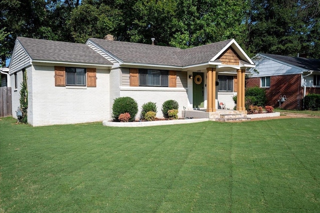 ranch-style home featuring a shingled roof, a front yard, brick siding, and a chimney