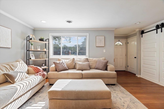 living room with visible vents, ornamental molding, a barn door, and wood finished floors