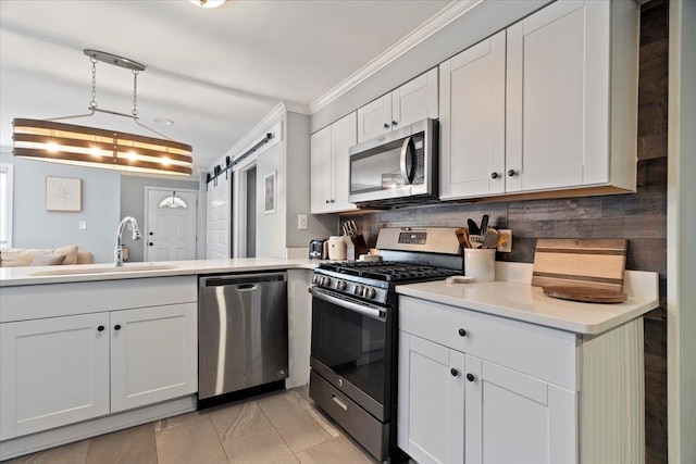 kitchen featuring ornamental molding, a sink, white cabinetry, a barn door, and appliances with stainless steel finishes