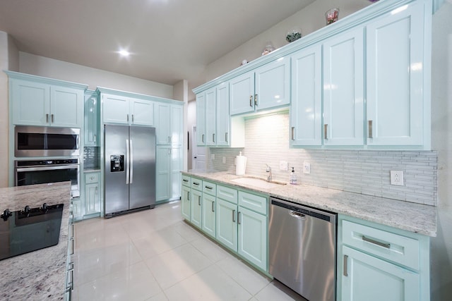 kitchen with light stone countertops, light tile patterned floors, appliances with stainless steel finishes, sink, and decorative backsplash