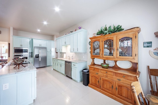 kitchen featuring light tile patterned floors, light stone counters, stainless steel appliances, white cabinetry, and tasteful backsplash