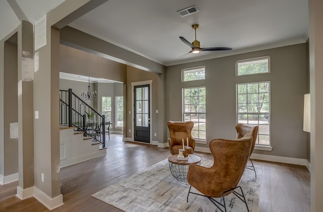 sitting room with ceiling fan with notable chandelier, wood-type flooring, and ornamental molding