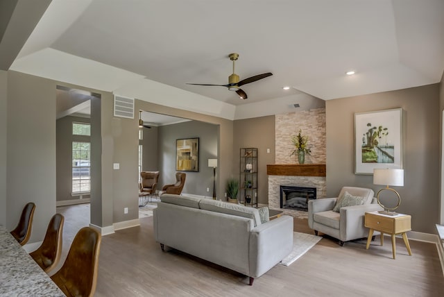 living room featuring ceiling fan, a stone fireplace, and light hardwood / wood-style floors