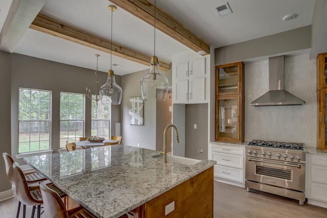 kitchen featuring high end stainless steel range, sink, beam ceiling, white cabinets, and wall chimney range hood