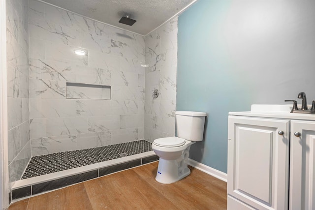 bathroom with vanity, toilet, hardwood / wood-style flooring, and a tile shower