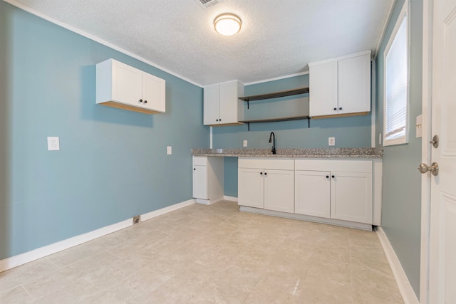 kitchen with a textured ceiling, sink, light stone countertops, and white cabinets