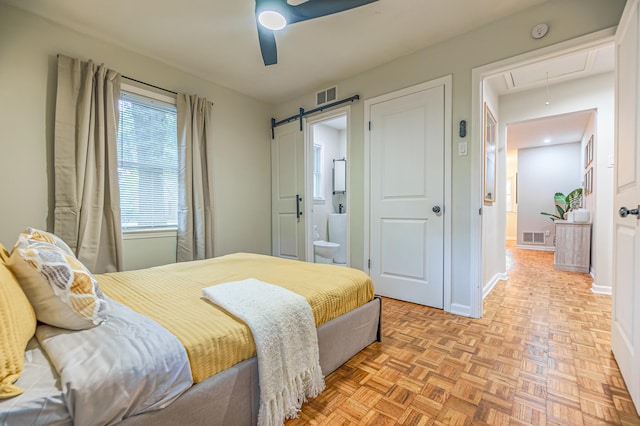 bedroom with a barn door, ceiling fan, light parquet floors, and ensuite bath