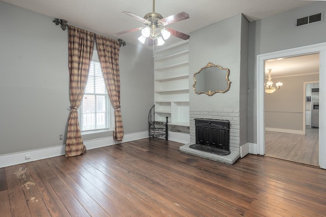 unfurnished living room with a textured ceiling, a brick fireplace, ceiling fan with notable chandelier, dark wood-type flooring, and ornamental molding