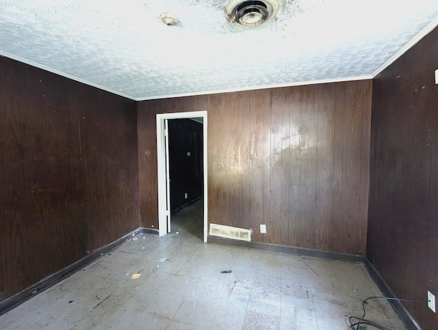 empty room featuring a textured ceiling, ornamental molding, and wooden walls