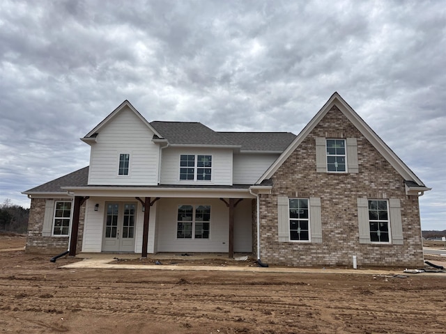 view of front of home with french doors, brick siding, and roof with shingles