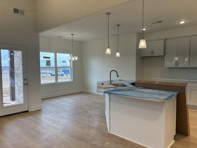 kitchen with sink, pendant lighting, an inviting chandelier, light hardwood / wood-style flooring, and an island with sink