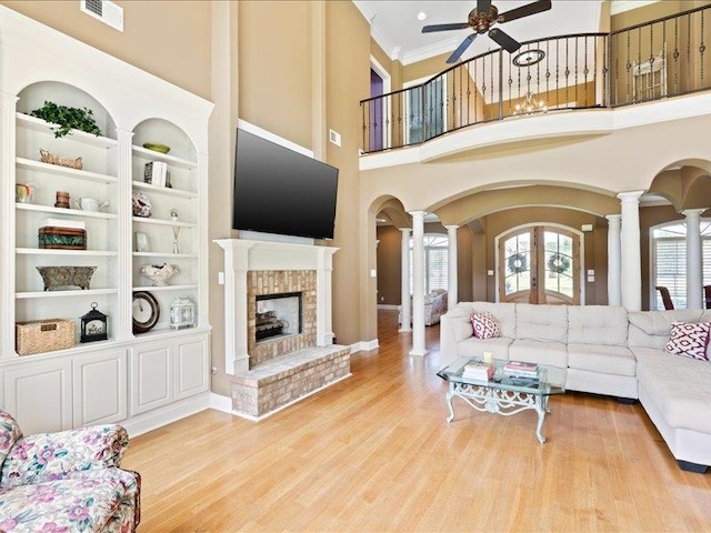 living room featuring light hardwood / wood-style flooring, ceiling fan, a brick fireplace, and ornate columns