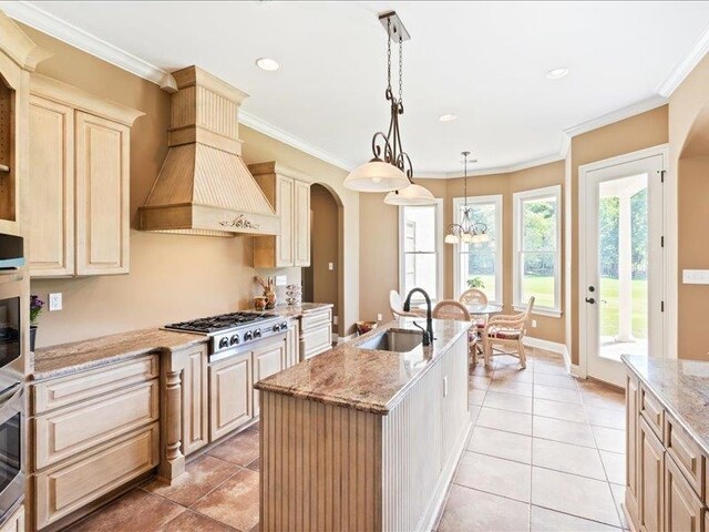 kitchen featuring a kitchen island with sink, hanging light fixtures, premium range hood, sink, and light stone countertops