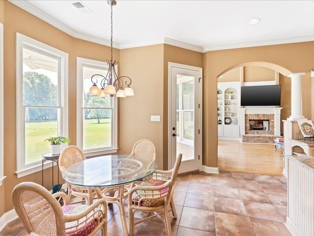 dining room with a fireplace, light hardwood / wood-style floors, a notable chandelier, decorative columns, and ornamental molding