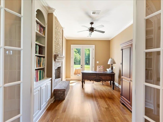 office featuring crown molding, french doors, light wood-type flooring, a brick fireplace, and ceiling fan