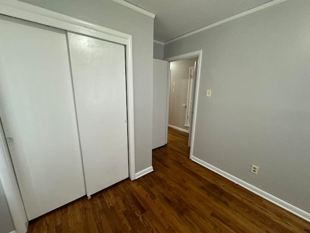 unfurnished bedroom featuring crown molding, dark wood-type flooring, and a closet