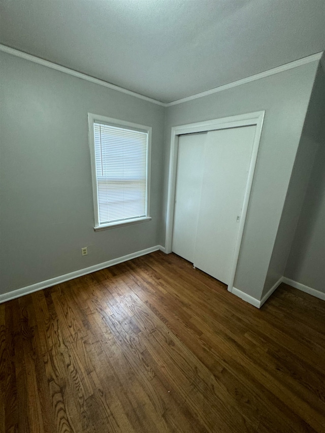 unfurnished bedroom with crown molding, dark wood-type flooring, and a closet