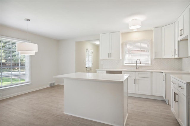 kitchen with hanging light fixtures, white cabinetry, a center island, sink, and decorative backsplash