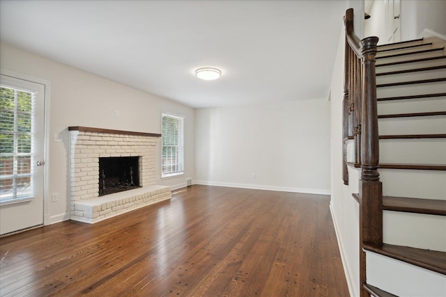 unfurnished living room featuring dark wood-type flooring and a brick fireplace