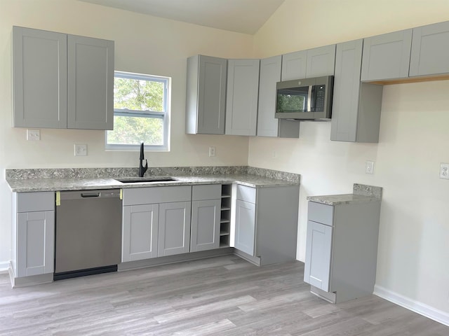 kitchen with vaulted ceiling, sink, appliances with stainless steel finishes, gray cabinetry, and light hardwood / wood-style floors