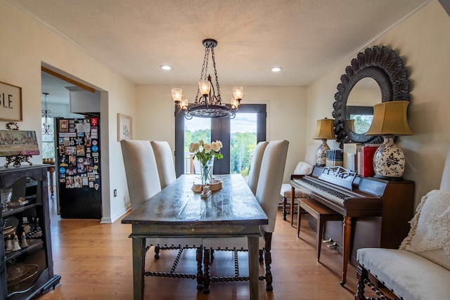 dining room with a textured ceiling, light hardwood / wood-style flooring, ornamental molding, and a notable chandelier