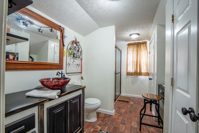 bathroom with a textured ceiling, vanity, toilet, and an enclosed shower