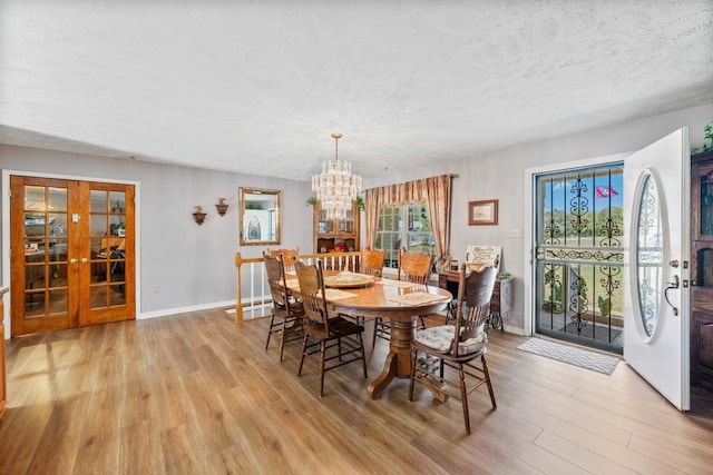 dining space with french doors, a textured ceiling, light hardwood / wood-style flooring, and an inviting chandelier