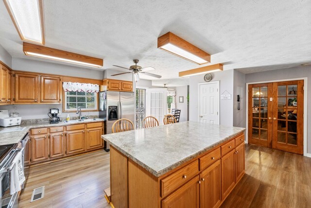 kitchen with a textured ceiling, stainless steel appliances, a kitchen island, ceiling fan, and light hardwood / wood-style floors