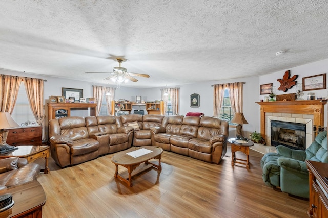 living room featuring ceiling fan, a textured ceiling, wood finished floors, and a tiled fireplace