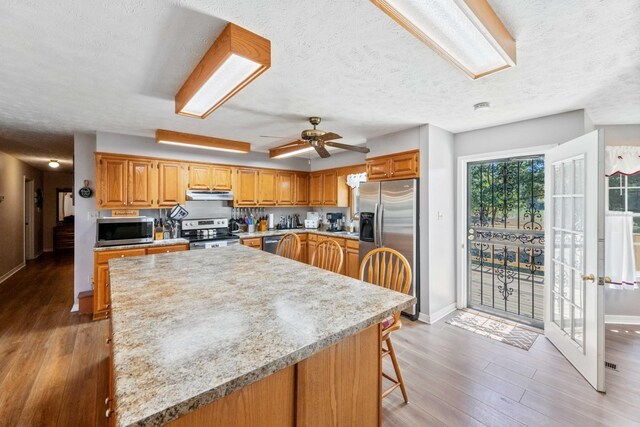 kitchen with hardwood / wood-style floors, appliances with stainless steel finishes, ceiling fan, a breakfast bar area, and a textured ceiling