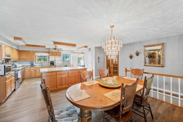 dining space featuring ceiling fan with notable chandelier, a textured ceiling, light hardwood / wood-style flooring, and sink