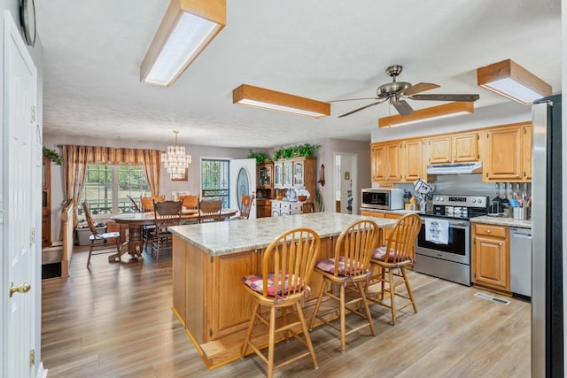 kitchen with a center island, light hardwood / wood-style flooring, ceiling fan with notable chandelier, stainless steel appliances, and a kitchen breakfast bar