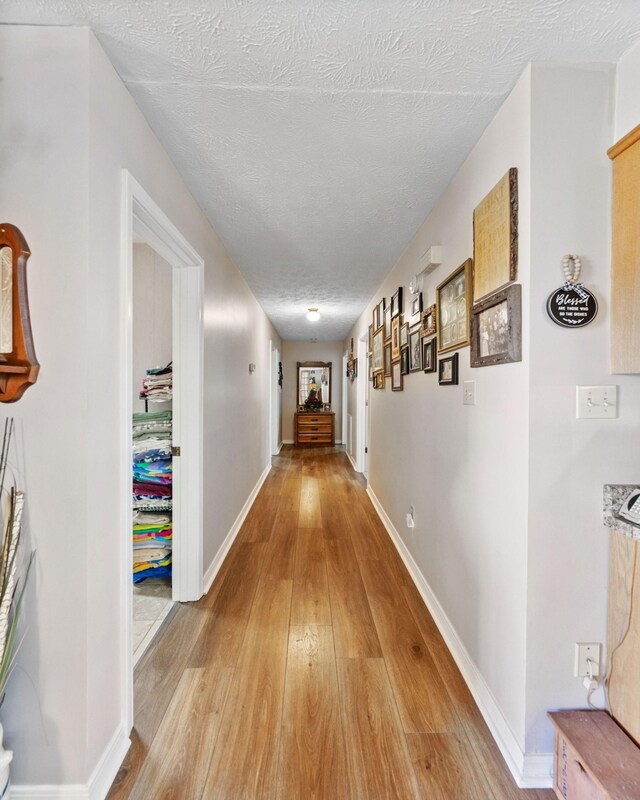 hallway with a textured ceiling and light hardwood / wood-style floors