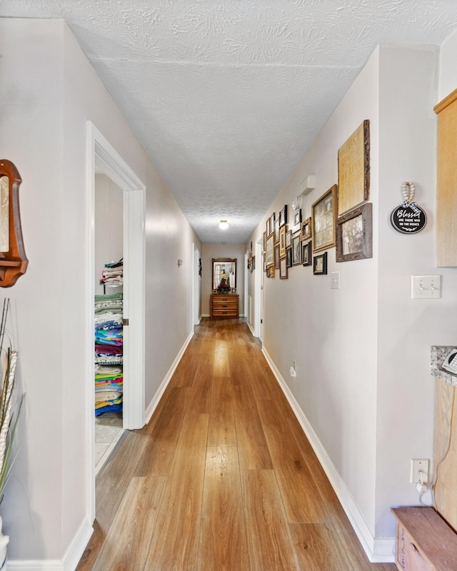 hall featuring baseboards, light wood-style floors, and a textured ceiling