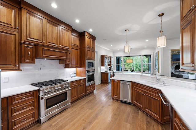 kitchen with light wood finished floors, ornamental molding, hanging light fixtures, stainless steel appliances, and a sink