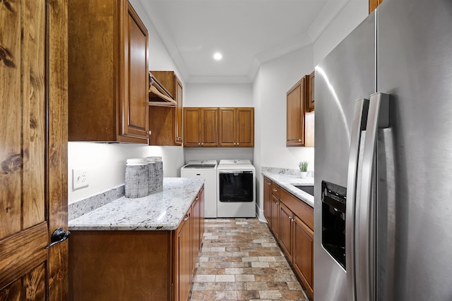 kitchen with ornamental molding, stainless steel refrigerator with ice dispenser, separate washer and dryer, brown cabinetry, and light stone countertops