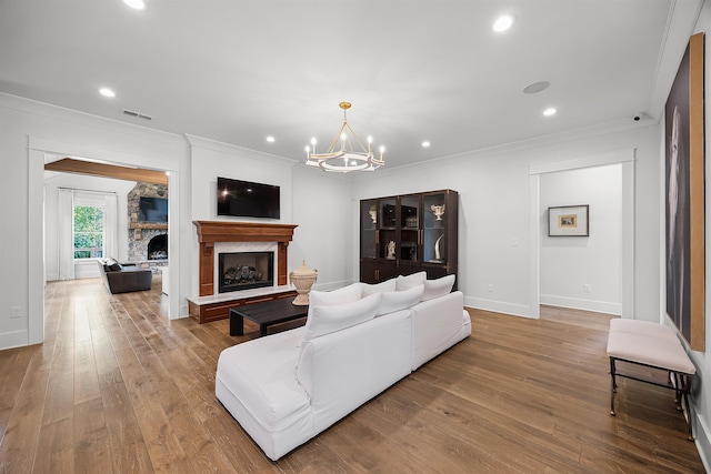 living area with visible vents, a fireplace with raised hearth, ornamental molding, hardwood / wood-style flooring, and a notable chandelier