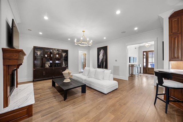 living area with visible vents, an inviting chandelier, a fireplace, ornamental molding, and light wood-style floors