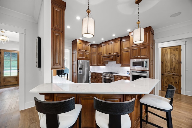 kitchen with brown cabinetry, a peninsula, premium appliances, ornamental molding, and light wood-type flooring