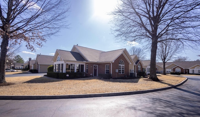 view of front facade featuring a residential view, brick siding, central AC, and driveway