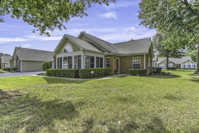 view of front of house featuring brick siding, a shingled roof, a front lawn, and a sunroom