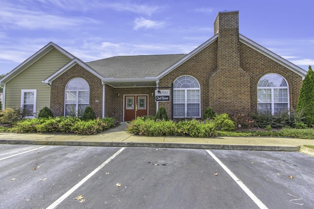 ranch-style home featuring brick siding, a chimney, roof with shingles, and uncovered parking