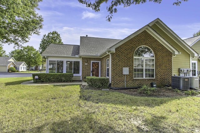 view of front of home with a front lawn, central air condition unit, brick siding, and roof with shingles