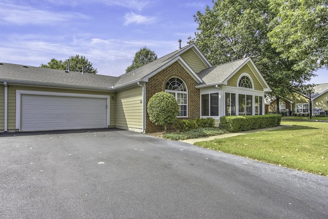 view of front of house featuring driveway, a shingled roof, a front lawn, a garage, and brick siding