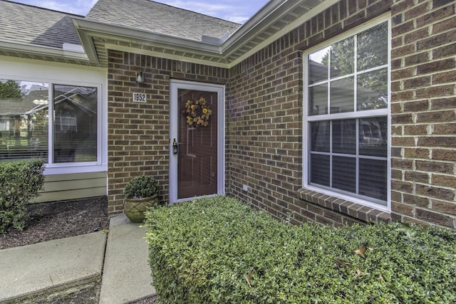 doorway to property featuring brick siding and roof with shingles