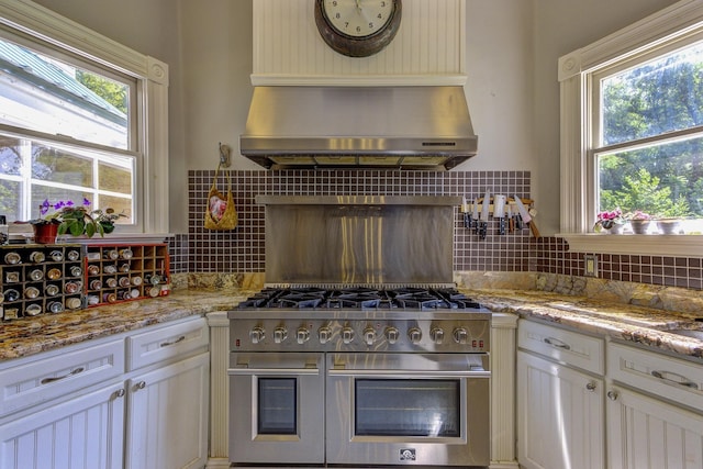 kitchen with backsplash, light stone countertops, wall chimney exhaust hood, and double oven range